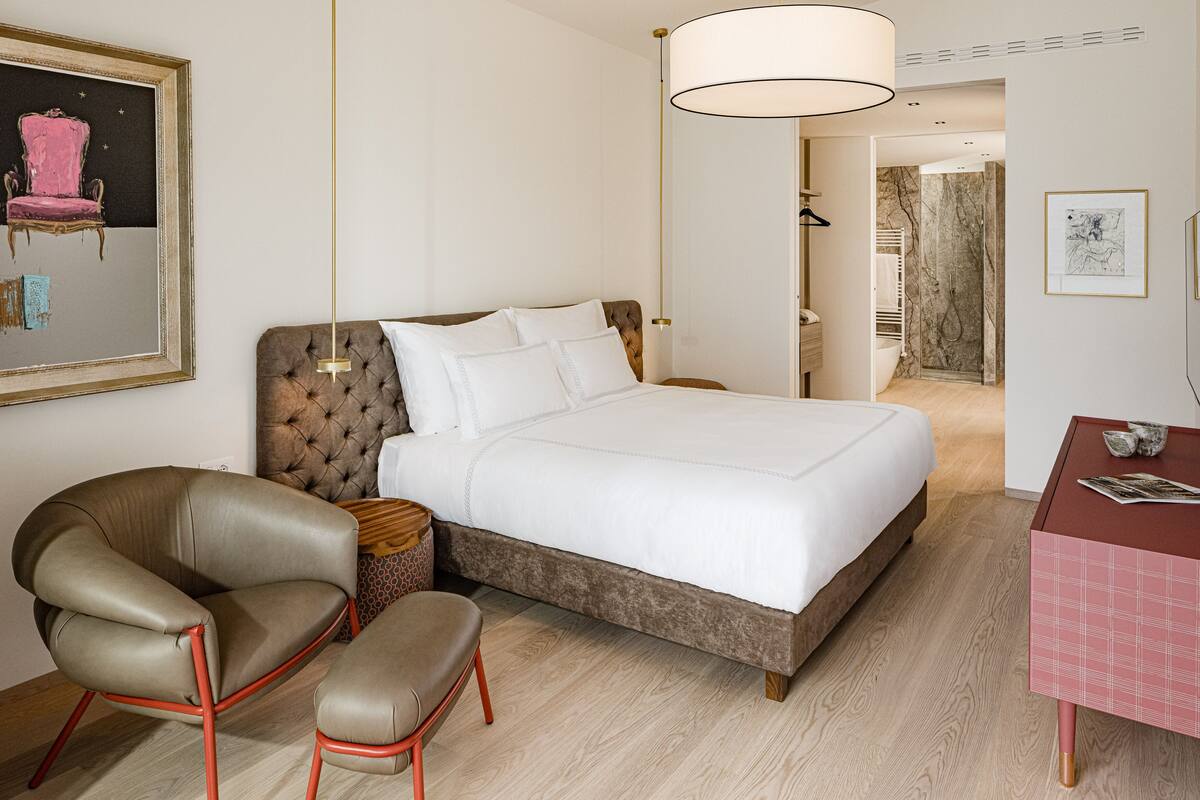 A hotel room with a large bed, a chair, a table, and a mirror.