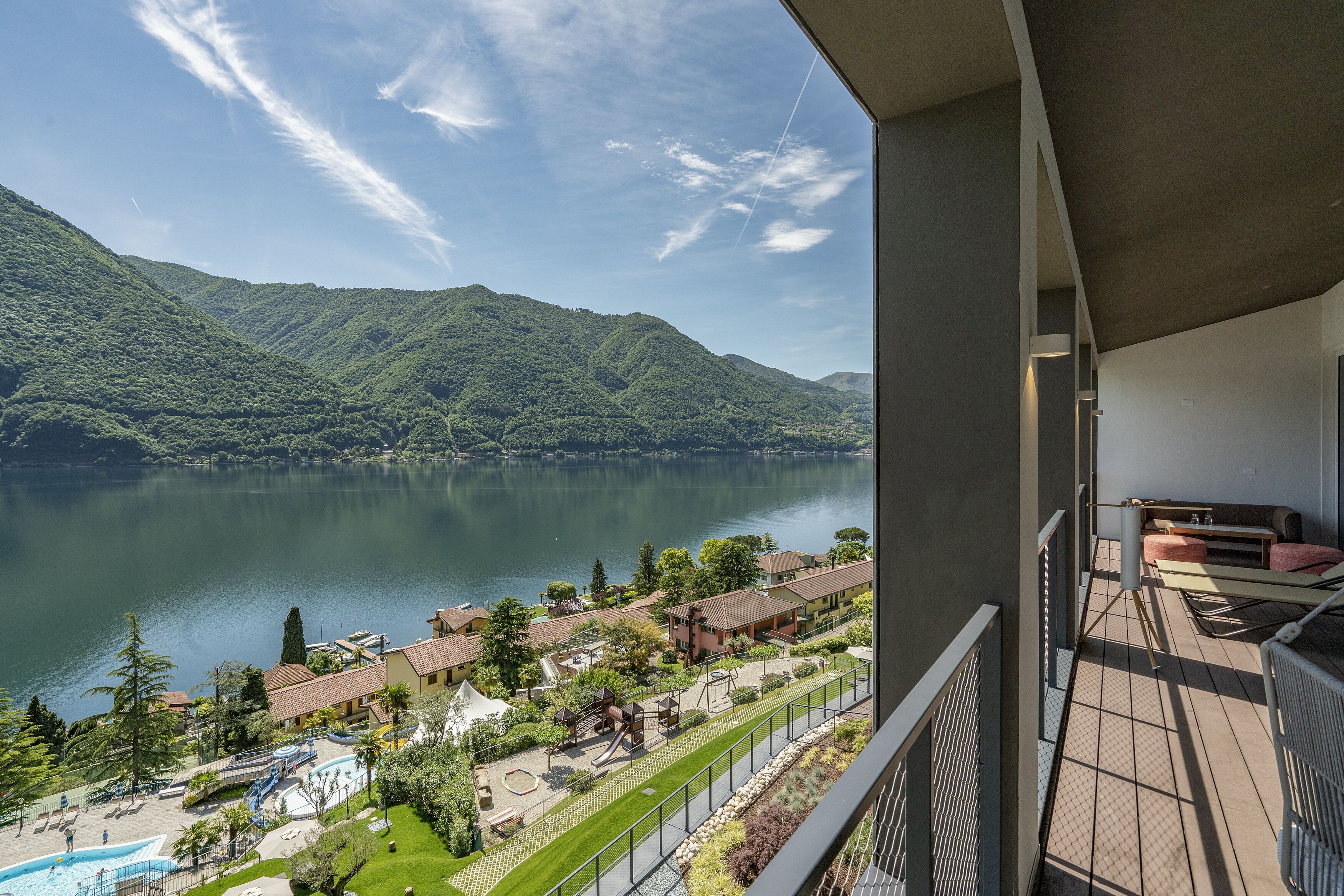 Un balcon offrant une vue sur un lac, des montagnes et une zone de villégiature avec des bâtiments et de la verdure.