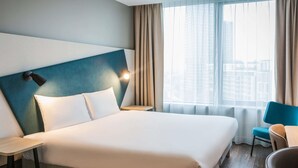 A hotel room with a large bed, a nightstand, a chair, and a window with curtains. - Aparthotel Adagio London Stratford (London)