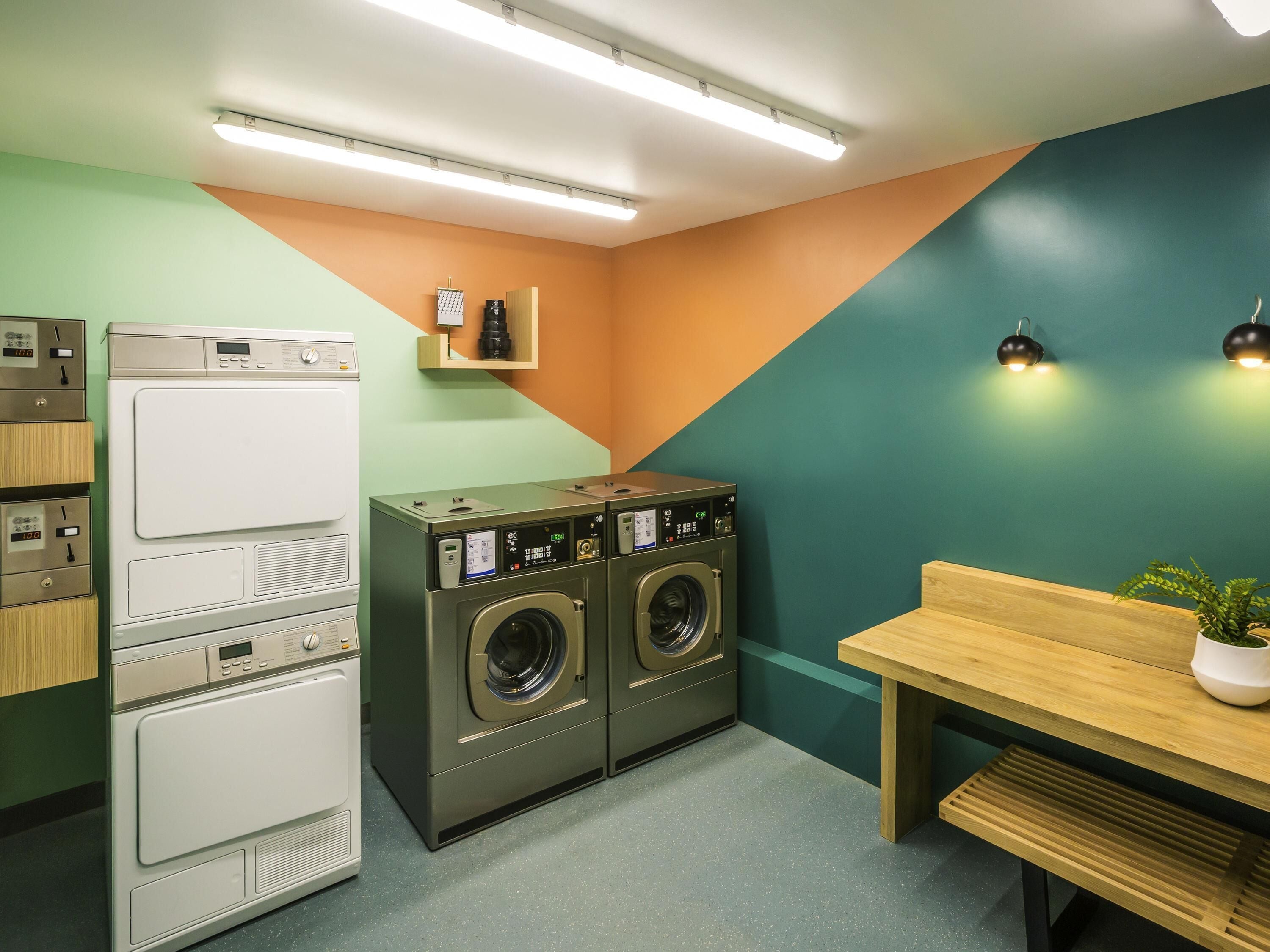 Une buanderie équipée d’une machine à laver et d’un sèche-linge superposés, d’une table en bois et d’une plante en pot.