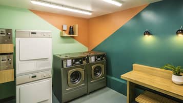 Une buanderie équipée d’une machine à laver et d’un sèche-linge superposés, d’une table en bois et d’une plante en pot.