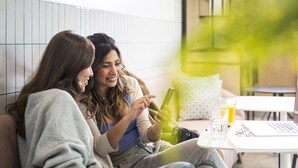 Two people sitting on a couch, one holding a smartphone, with a laptop and a glass of orange juice on a small table beside them. - Aparthotel Adagio London Stratford (London)