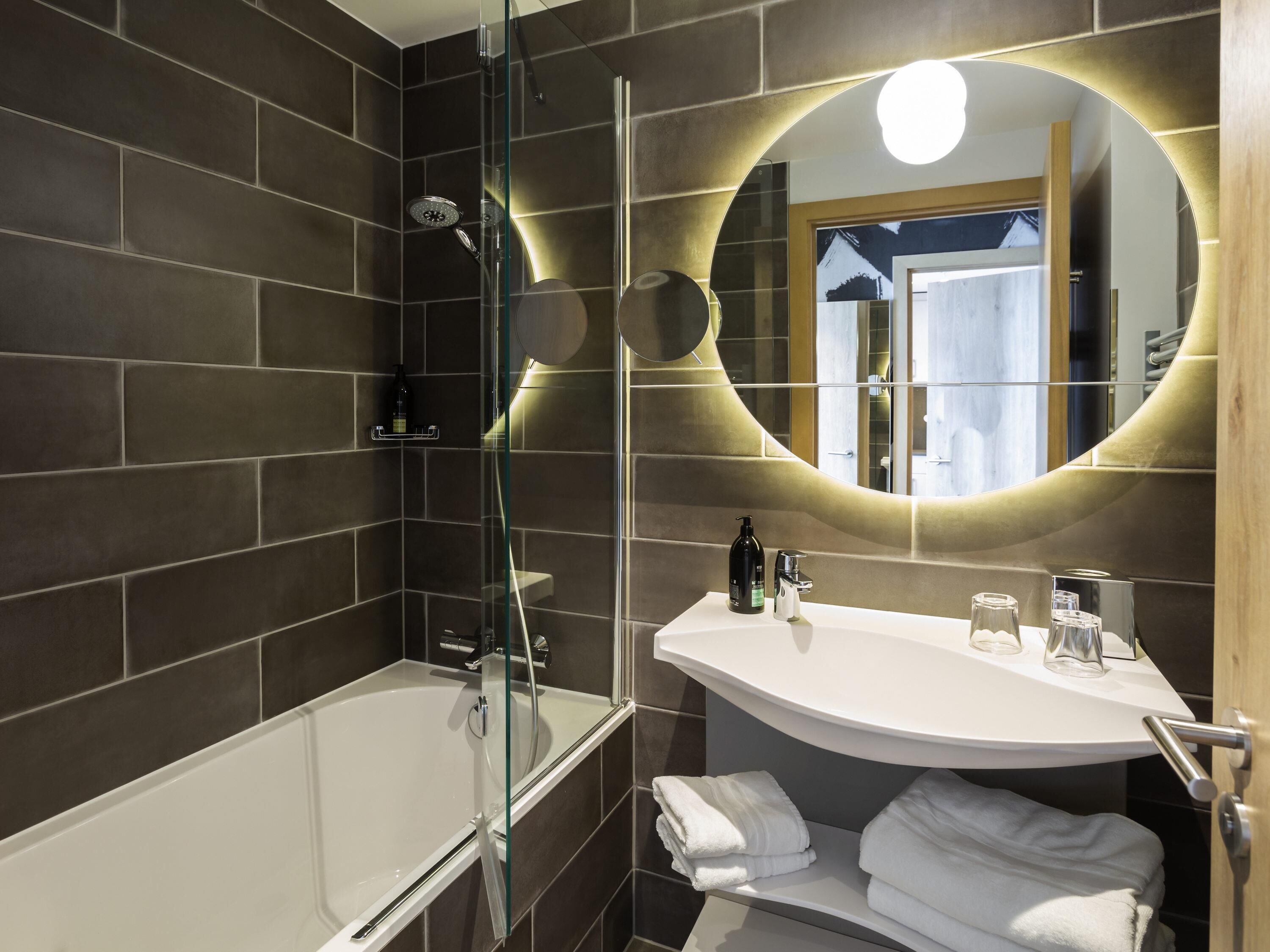 A modern bathroom with a glass-enclosed shower, a white sink with a mirror, and neatly folded towels.
