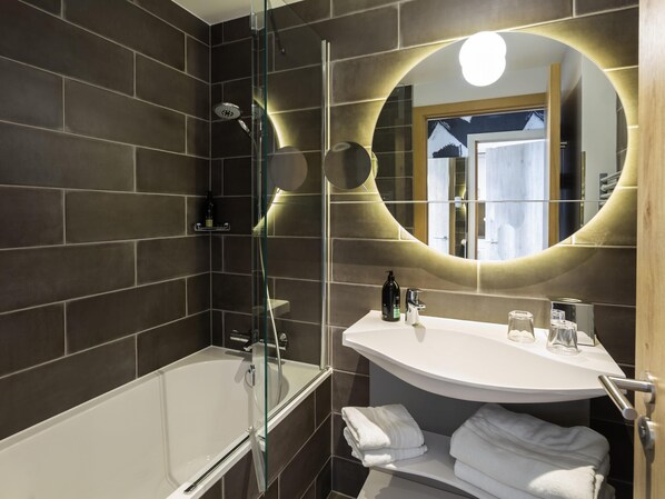 A modern bathroom with a glass-enclosed shower, a white sink with a mirror, and neatly folded towels.