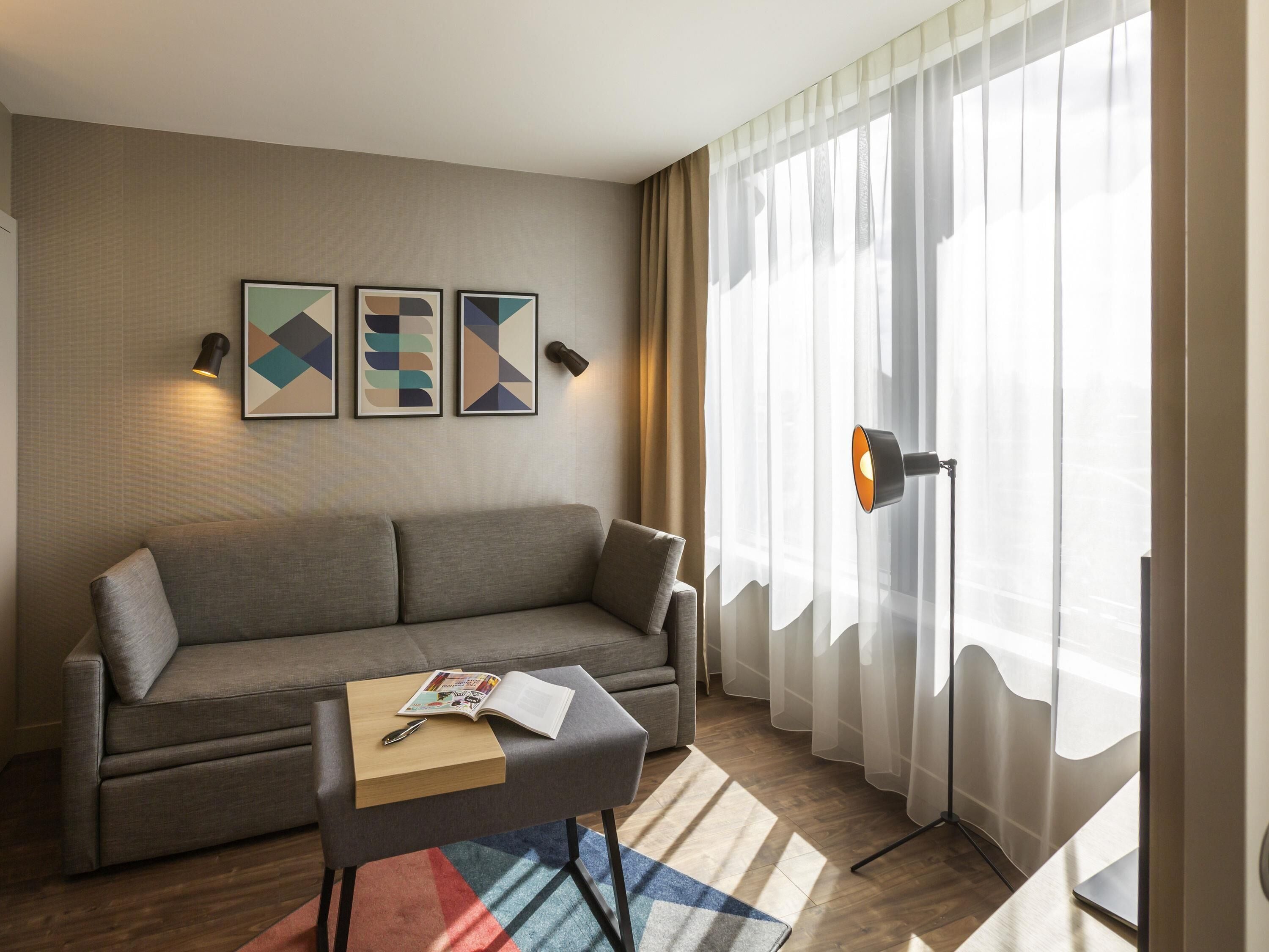 Un salon moderne avec un canapé, une petite table sur laquelle se trouvent un livre et un stylo, des œuvres d’art abstraites accrochées au mur et une lampe sur pied.