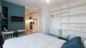 A modern bedroom with a large bed, a desk, and a kitchenette in the background. - "Blue Dream" – Cozy, clean & stylish studio | Doua / INSA / CESI - Garage, WIFI (Villeurbanne)