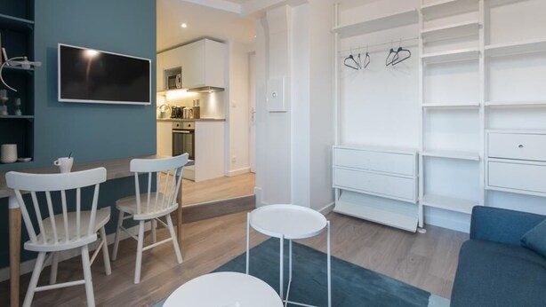 A modern living room with a TV, white chairs, a small table, and a blue sofa. - "Blue Dream" – Cozy, clean & stylish studio | Doua / INSA / CESI - Garage, WIFI (Villeurbanne)