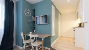 Un espace de vie compact comprenant un coin repas, un téléviseur fixé au mur et une petite cuisine.