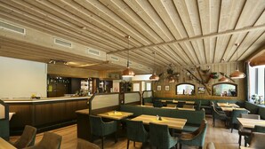 A restaurant with wooden ceiling beams, green upholstered booths, and a bar area.