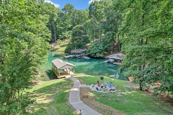 Escape to a serene lakeside retreat with a wooden dock, gazebo, and fire pit surrounded by lush greenery.