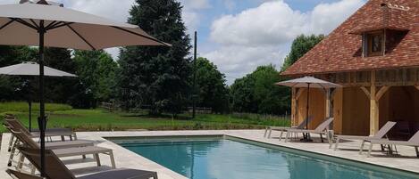 A swimming pool with lounge chairs and umbrellas, surrounded by a wooden building and greenery.