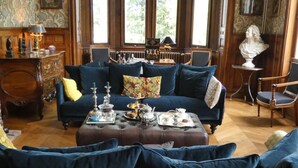A traditional room with a dark blue sofa set, a wooden coffee table with tea service, and a bust sculpture on a side table. - Chateau de Hieville (Saint-Pierre-en-Auge)