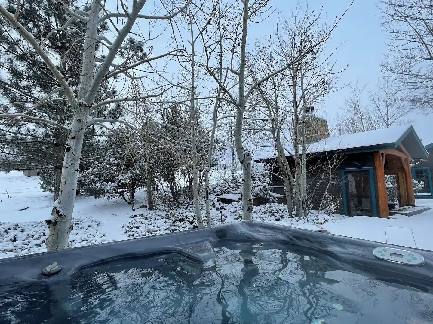 A hot tub in a snowy outdoor area with a wooden structure in the background.