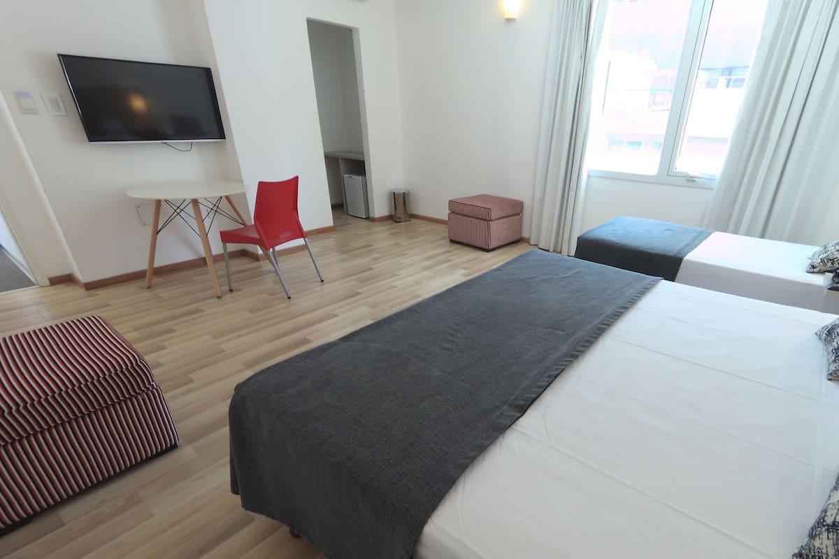 A hotel room with a bed, a TV, a desk, a chair, and a window.