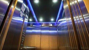 Interior de un ascensor con paredes metálicas, un panel de control y luces en el techo.
