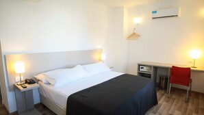 Una habitación de hotel con cama, mesitas de noche, escritorio, silla y aire acondicionado.