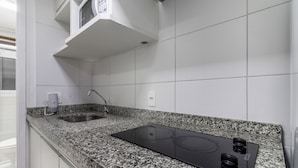 A kitchen with white tiles, a granite countertop, a stainless steel sink, and a black induction cooktop. - AV1110 - Studio 4 guests Avanhandava Street (São Paulo)