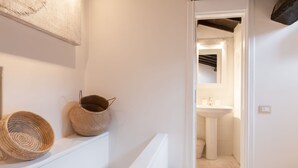 A hallway leading to a bathroom with a sink and mirror. There are two woven baskets on a shelf.