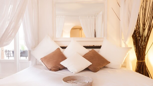 A neatly made bed with white and brown pillows, a woven basket, and a mirror above.