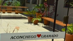 A sign with the text "Aconchego Gramado" in a courtyard with potted plants and outdoor seating. - Locar-in Gramado - Aconchego Coração de Gramado (Gramado)