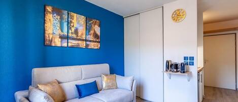 Un salón moderno con una pared azul decorativa, un sofá blanco y una mesa de centro de vidrio.