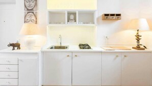 A white kitchen with a sink, cabinets, a small shelf with decorative items, and a wall-mounted shelf above the sink. - COLOSSEO HISTORIC APARTMENT (Roma)