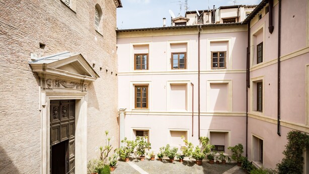 A courtyard with a brick building, a wooden door, and potted plants. - COLOSSEO HISTORIC APARTMENT (Roma)