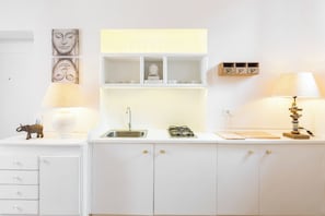 A kitchen with a sink, cabinets, a small shelf with cups, and a decorative elephant figurine.