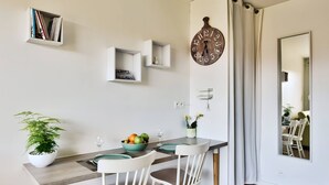 Ein Essbereich mit Holztisch, weißen Stühlen, einem Blumentopf und einer Wanduhr.