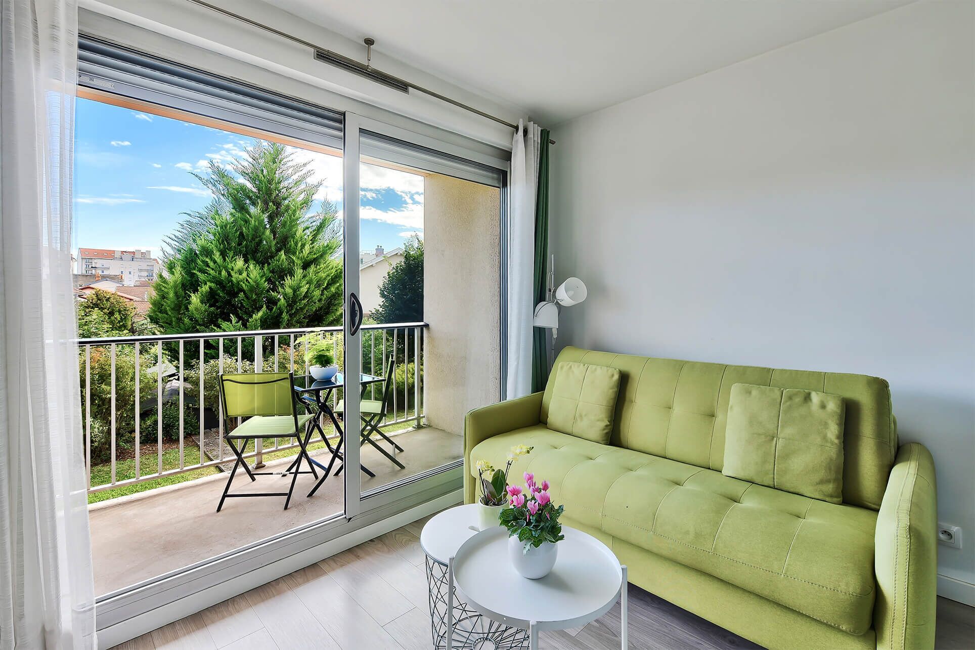 A balcony with a green sofa, a small table with a flower pot, and a chair.