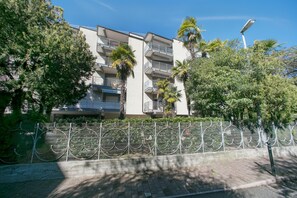 A multi-story building with balconies, surrounded by trees and a decorative fence.