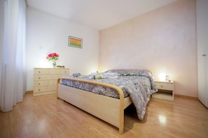 A bedroom with a bed, wooden dresser, bedside table, and a wall-mounted picture.