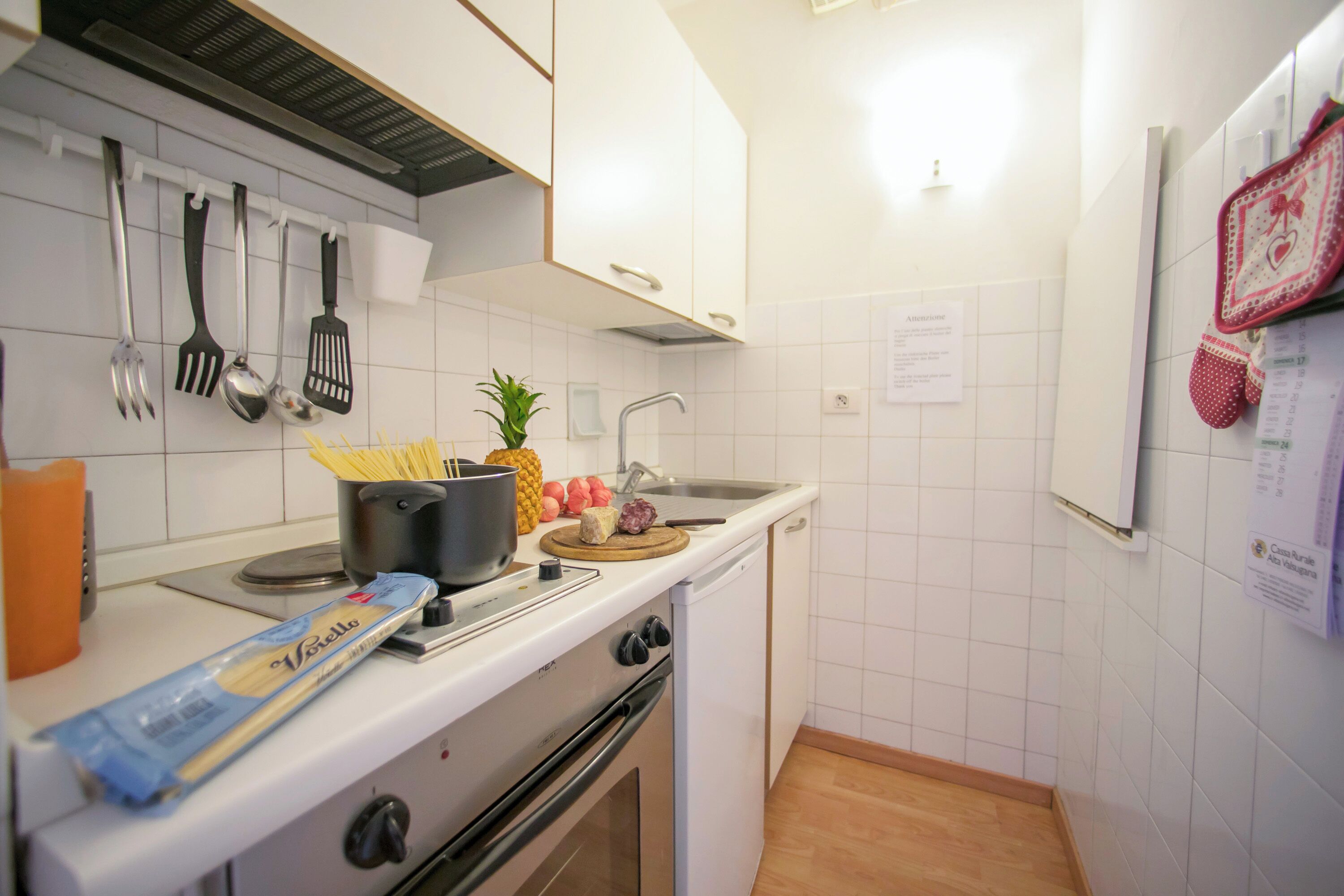 Une cuisine avec des meubles blancs, une cuisinière, un évier et divers ustensiles.