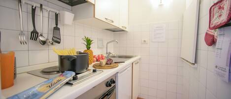Une cuisine avec des meubles blancs, une cuisinière, un évier et divers ustensiles.