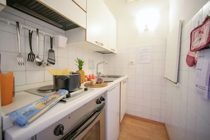 A kitchen with white cabinets, a stove, a sink, and various utensils.