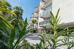 A multi-story building with balconies, surrounded by greenery and palm trees.
