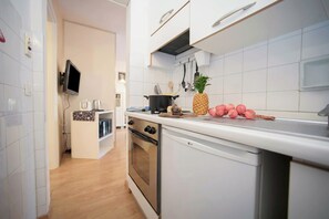 A modern kitchen with white cabinets, a stainless steel oven, and a flat-screen TV mounted above the counter. - Riva Lago e Spiaggia Apartment (Riva del Garda)
