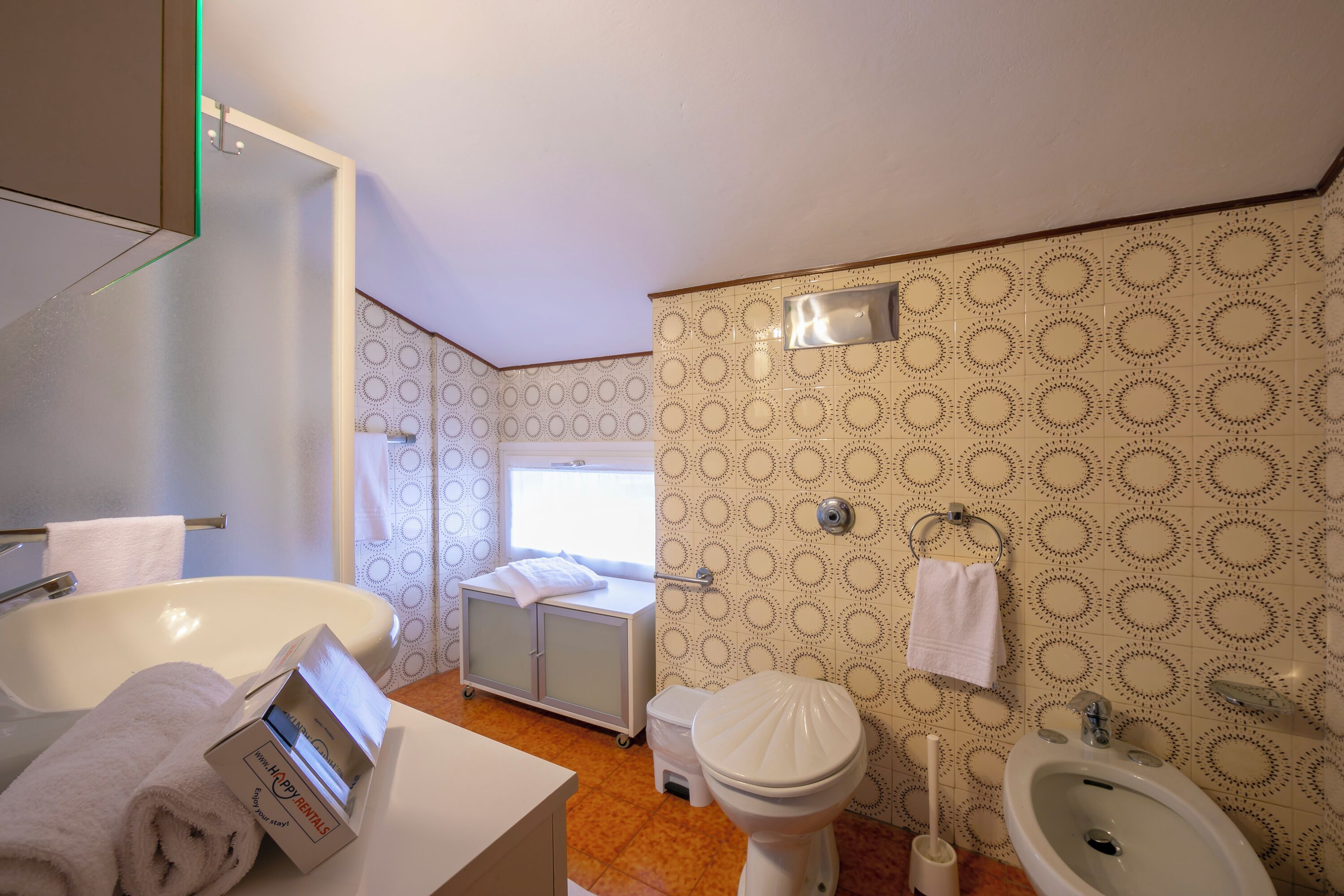 Un baño con lavamanos, inodoro y bidé blancos, un espejo y paredes con diseño.