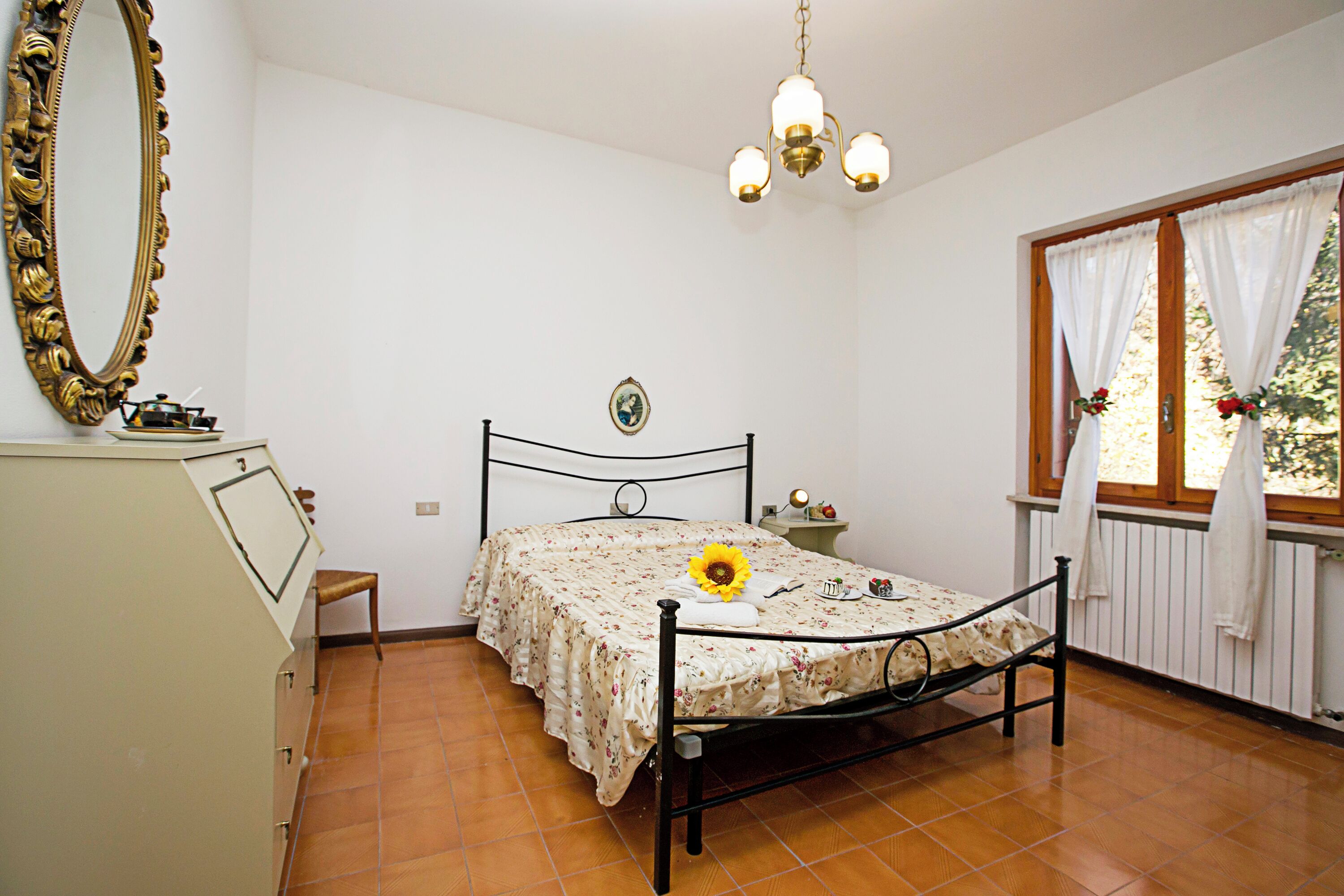 A bedroom with a bed, a dresser, a mirror, a chandelier, and a window with curtains.