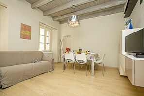A living room with a sofa, dining table, chairs, a TV, and a chandelier. - Residenza Il Cavaliere del Lago (Riva del Garda)