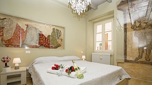 Hotellihuone, jossa on suuri sänky, yöpöytä lampun kanssa, ikkuna, josta on näkymä, ja seinä, jossa on suuri taulu.