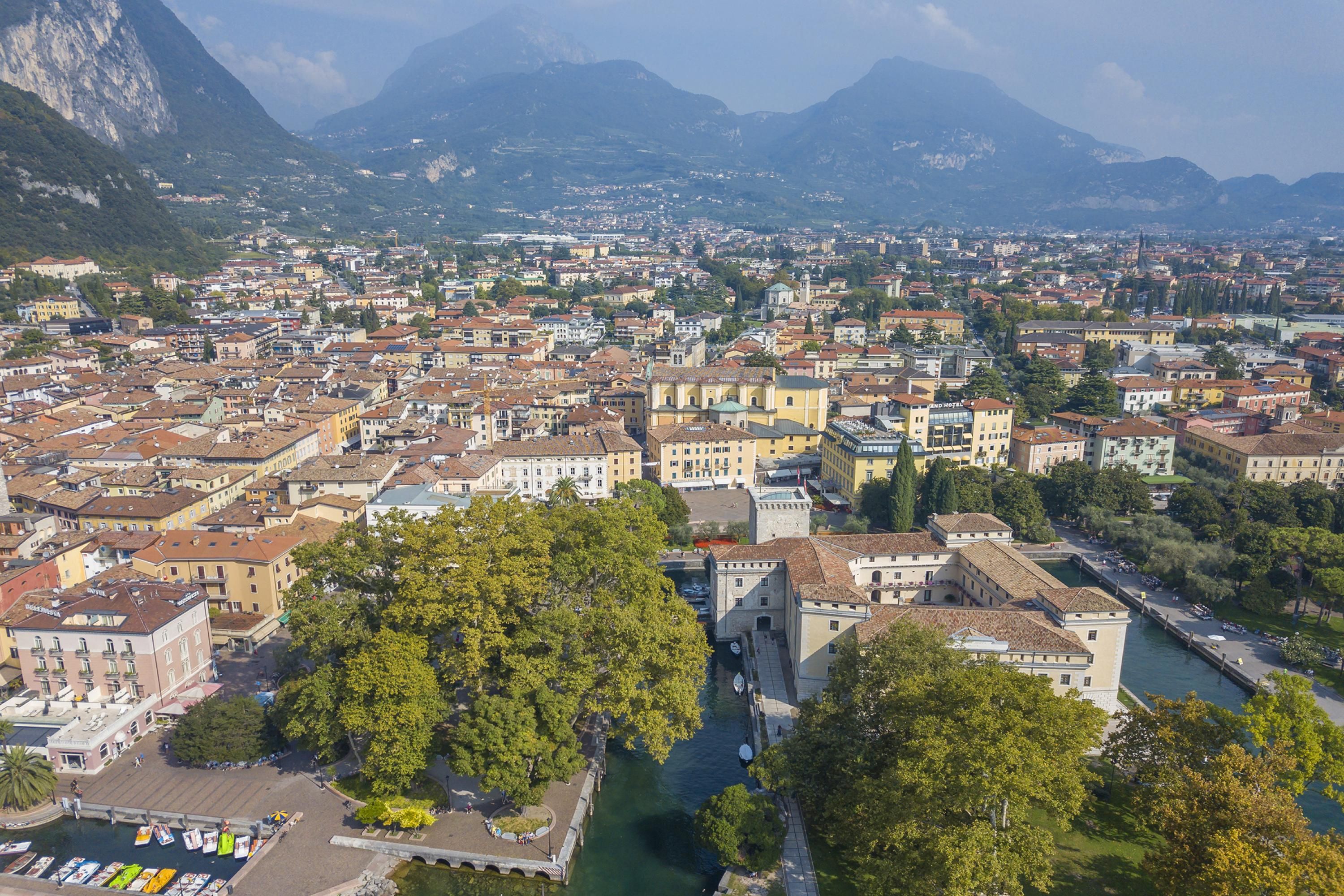 A panoramic view of a historic town with a river, buildings, and mountains in the background.