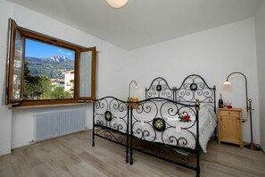 Um quarto com cama, janela, radiador, mesa de cabeceira e abajur.