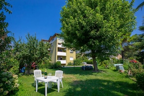 Um jardim com uma mesa e cadeiras, uma garrafa de vinho e um edifício ao fundo.