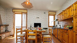 Une cuisine avec des meubles en bois, une table à manger avec des chaises, un téléviseur et une cheminée.