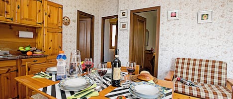 A dining area with a wooden table set for a meal, a sofa, and a kitchen area with wooden cabinets.