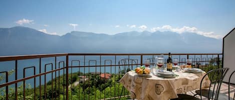 Una terraza con mesa dispuesta para comer, con vistas a un paisaje montañoso y una masa de agua.