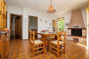 Una cocina con una mesa de comedor, sillas, una lámpara colgante, una chimenea y papel tapiz estampado.