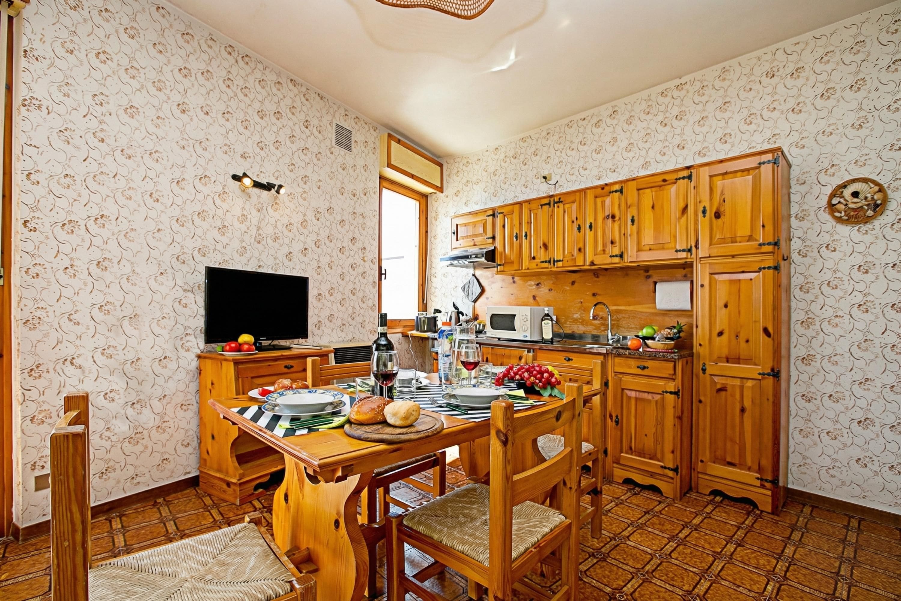 A kitchen with wooden cabinets, a dining table, chairs, a television, and a microwave.