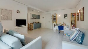 A modern living room with a flat-screen TV, a sofa, a dining table, and a kitchen area in the background. - Riva Lago e Spiaggia Apartment 3 (Riva del Garda)